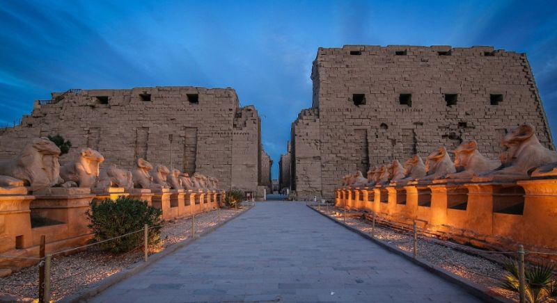 Recinto sagrado al atardecer con esfinges y obeliscos.